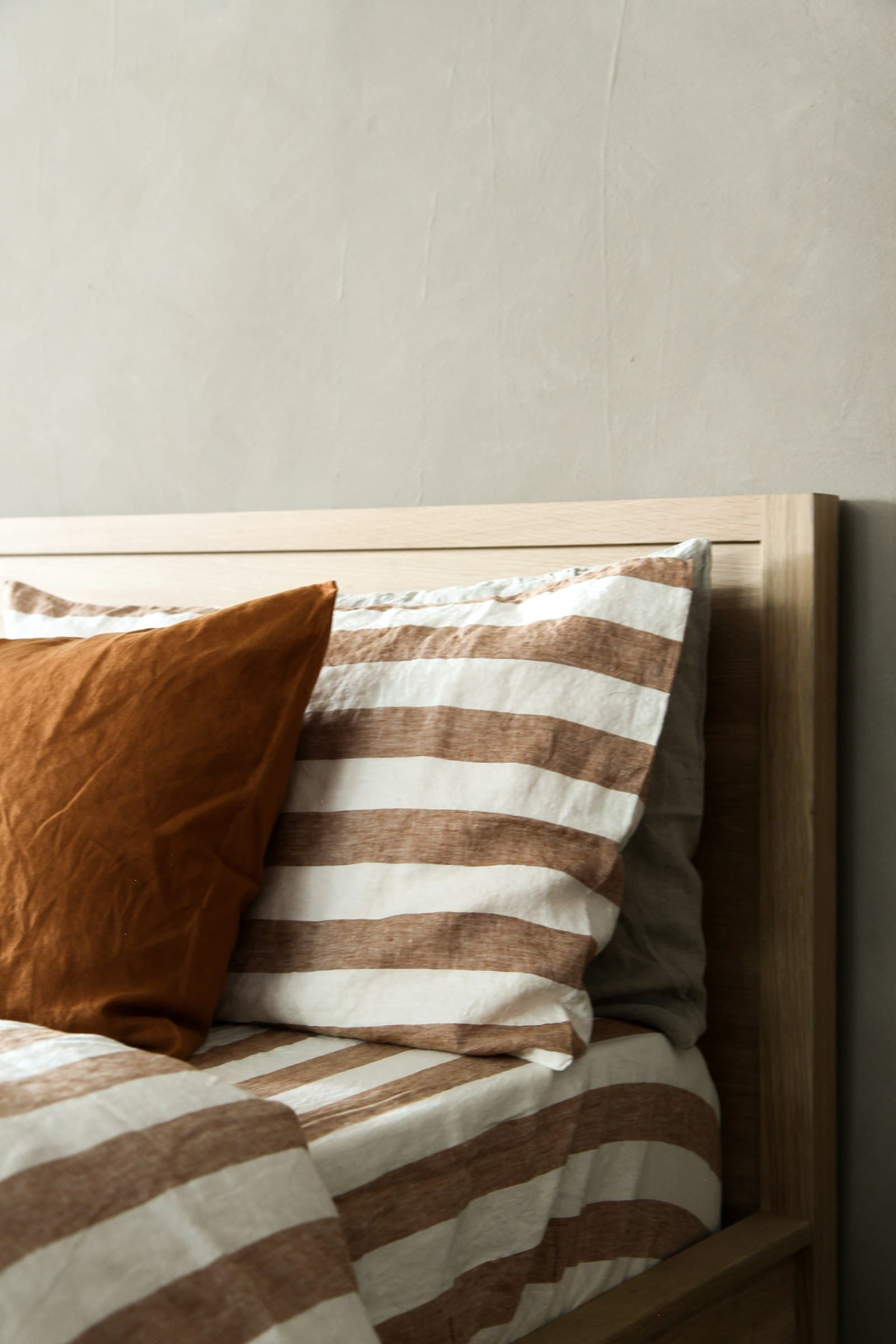 A rust-striped linen cushion against natural bedlinen