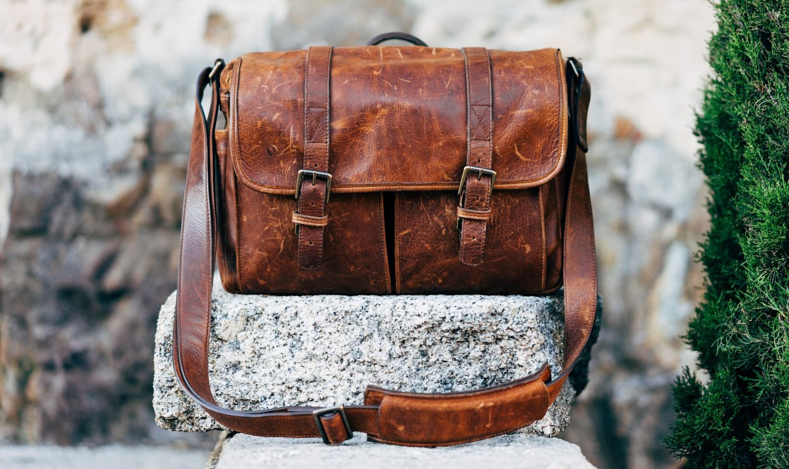 A hand-stitched tan leather satchel with brass buckles, resting on a stone step outside the Whitchurch workshop