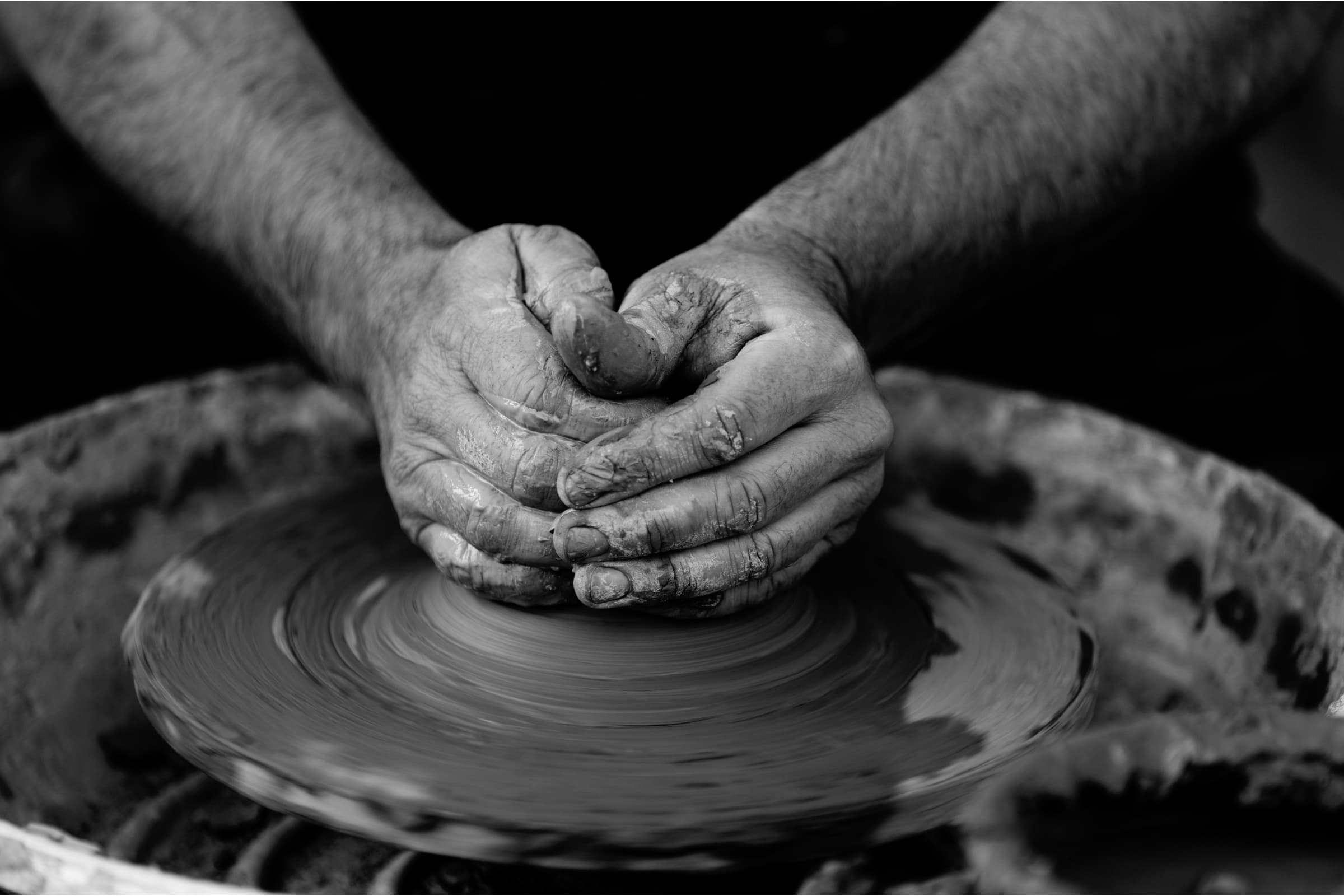 Clay-covered hands shaping a pot on a pottery wheel